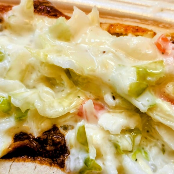Close-up of a hot dog with chili and creamy coleslaw in a bun.