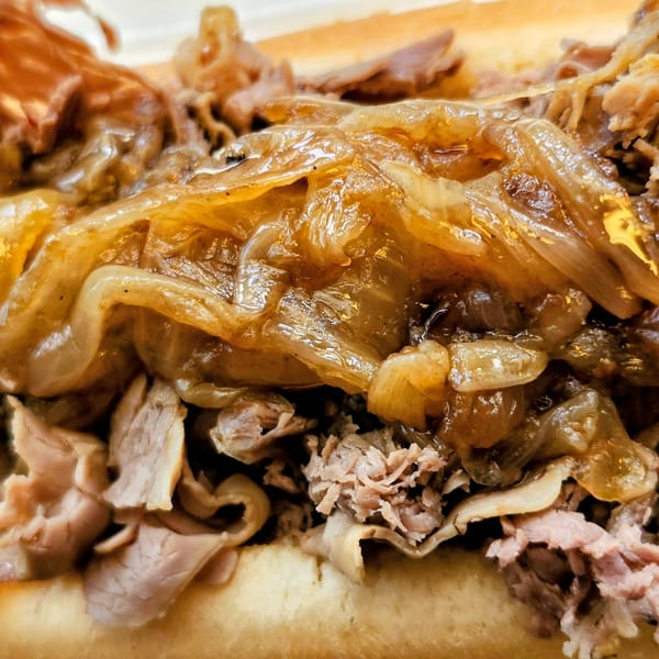 Close-up of a cheesesteak sandwich overflowing with thinly sliced meat and caramelized onions.