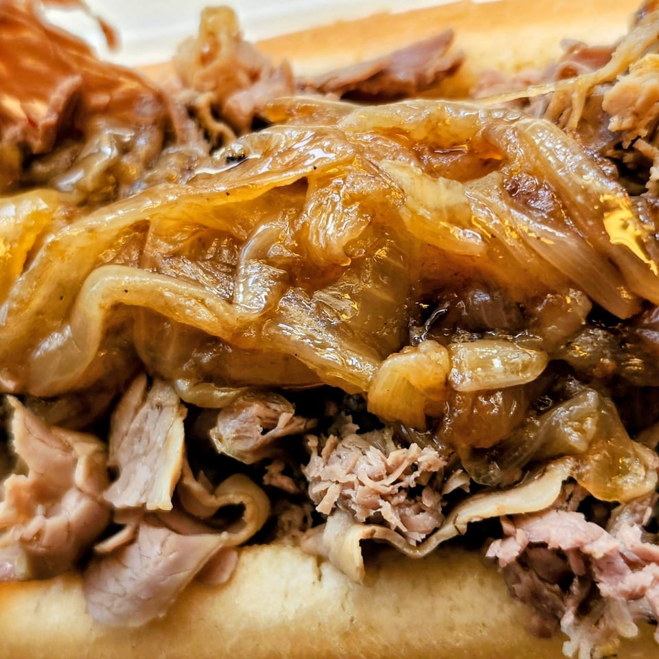 Close-up of a cheesesteak sandwich overflowing with thinly sliced meat and caramelized onions.