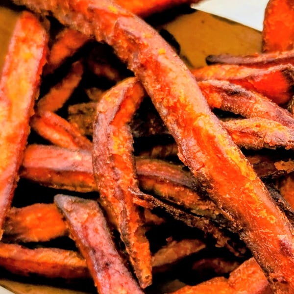 Close-up of crispy, golden-orange sweet potato fries piled together.