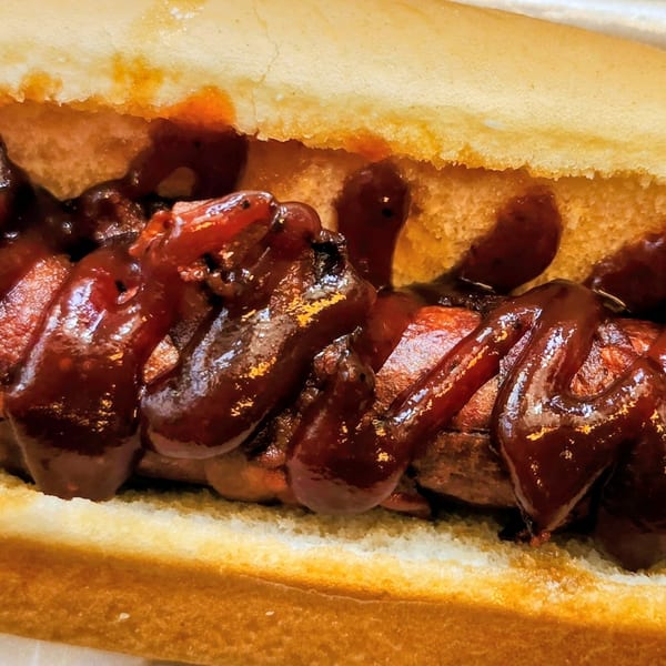 Close-up of a hot dog in a bun, generously topped with dark, glistening barbecue sauce.