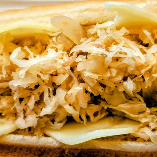 Close-up of a hot dog in a bun, topped with sauerkraut, melted cheese, and mustard.