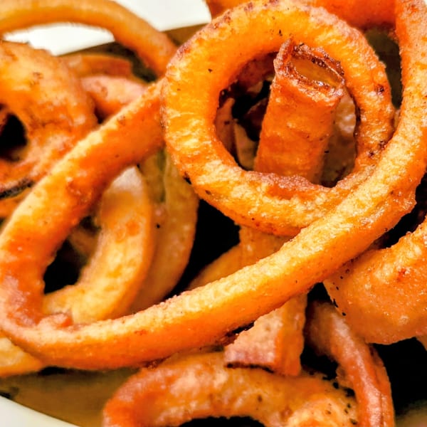 Close-up of golden-brown curly fries, some with visible seasoning, in a white container.