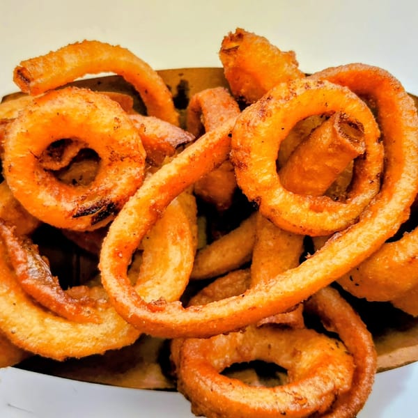 A close-up of a brown paper container filled with golden-brown, crispy curly fries.