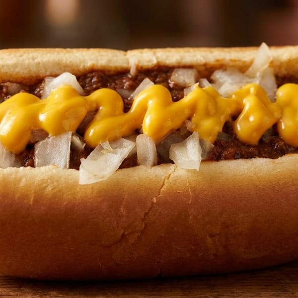 Chili cheese hot dog with diced onions and mustard on a wooden surface.