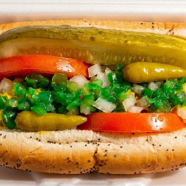A Chicago-style hot dog in a poppy seed bun with mustard, relish, onions, tomatoes, pickle spear, and peppers.
